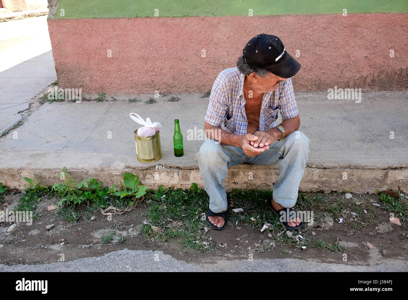 Scène de rue à Trinidad, Sancti Spiritus, Cuba. Cubaine locale homme assis sur le trottoir avec de la bière et un peut. La pauvreté et la solitude. Banque D'Images