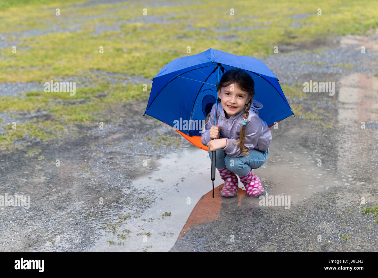 Petite fille jouant dans la pluie parapluie sous Banque D'Images