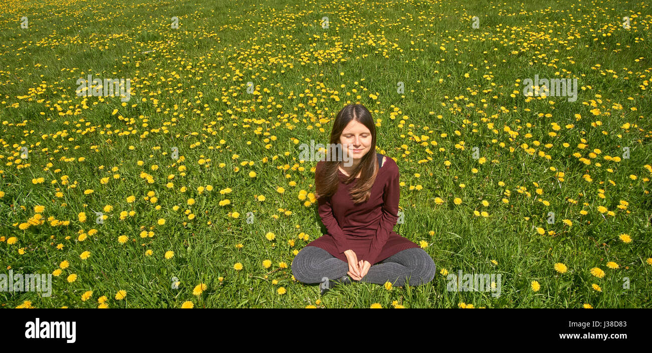 Belle jeune femme de détente sur une prairie avec beaucoup de pissenlits dans le soleil du printemps. Vue frontale avec copyspace. Banque D'Images