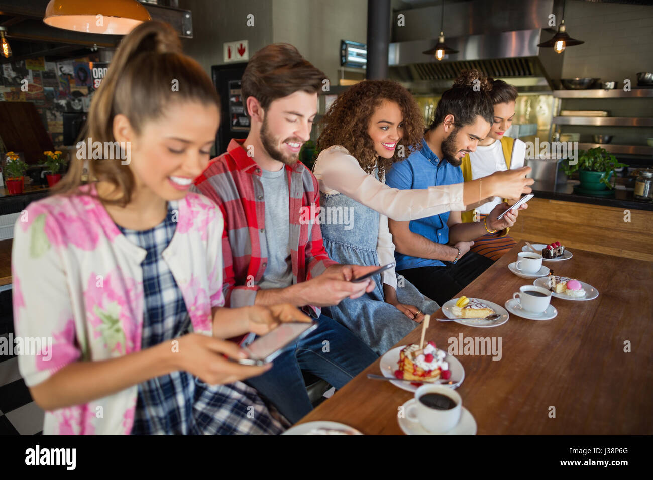 Smiling friends en utilisant leur téléphone mobile en position assise par les tasses de café et desserts sur la table in restaurant Banque D'Images