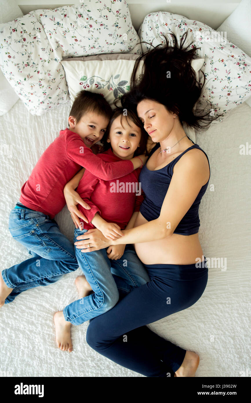 Belle jeune mère enceinte et ses deux enfants, des garçons, lyign au lit à la maison Banque D'Images