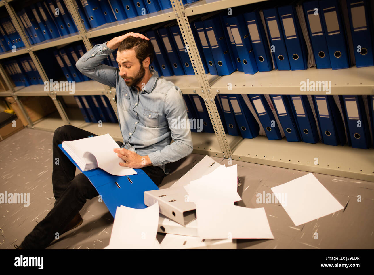 Homme d'affaires fatigué avec des papiers éparpillés dans le fichier de travail Banque D'Images