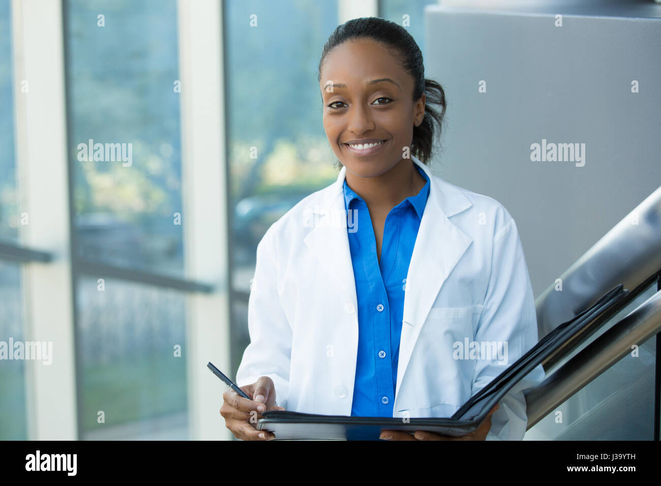 Closeup portrait portrait de friendly, smiling confident female doctor, professionnel de la santé avec labcoat, enclos à face et holding notebook Banque D'Images