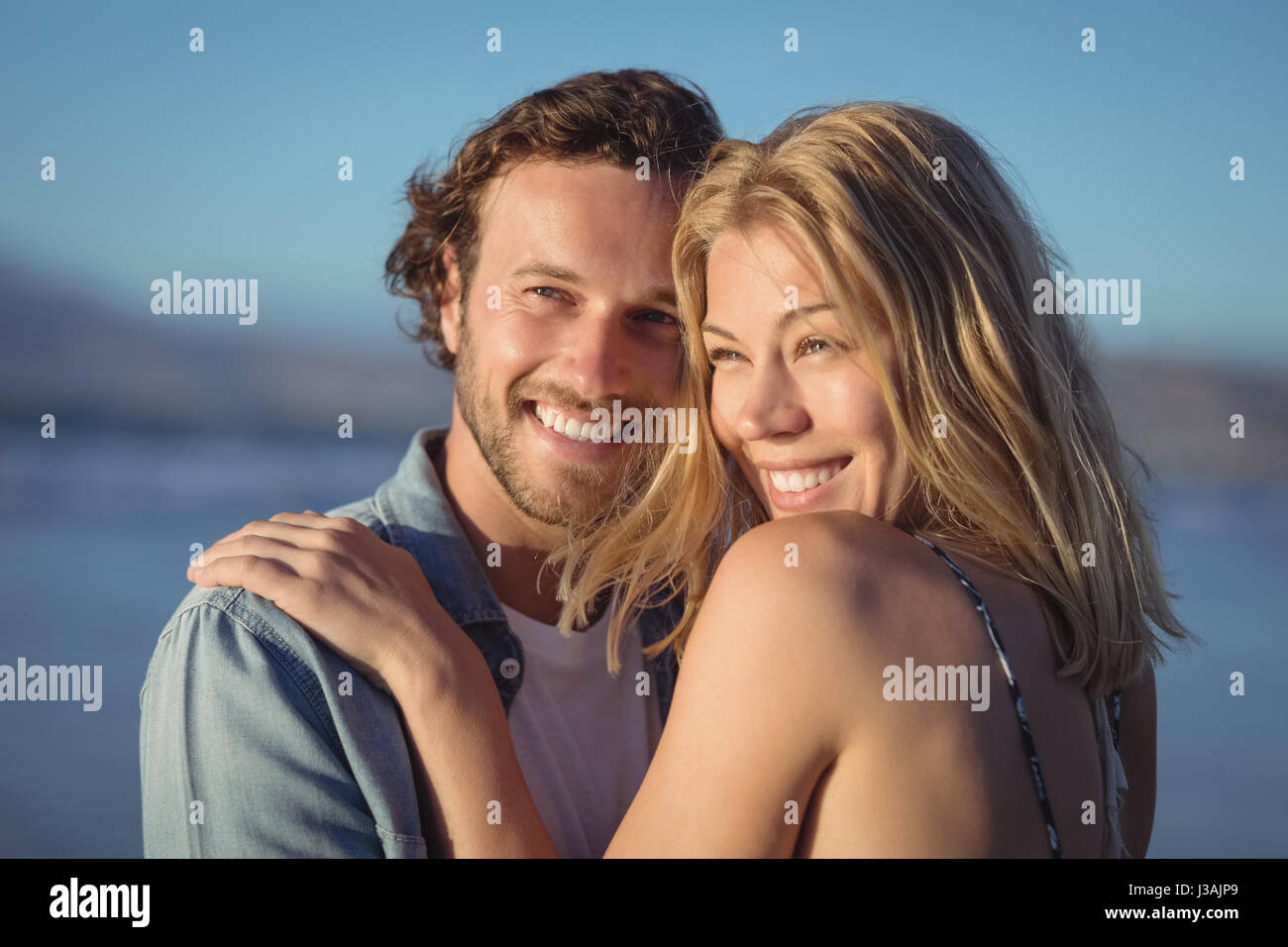 Thoughtful couple hugging at beach au cours de journée ensoleillée Banque D'Images