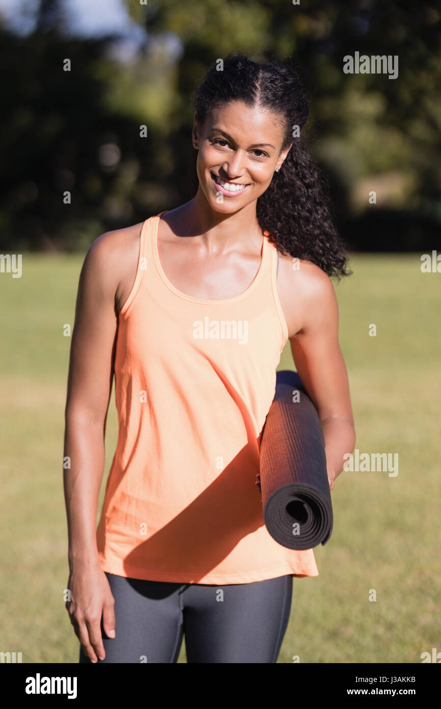 Portrait of happy young woman holding tapis d'exercice au parc sur sunny Banque D'Images