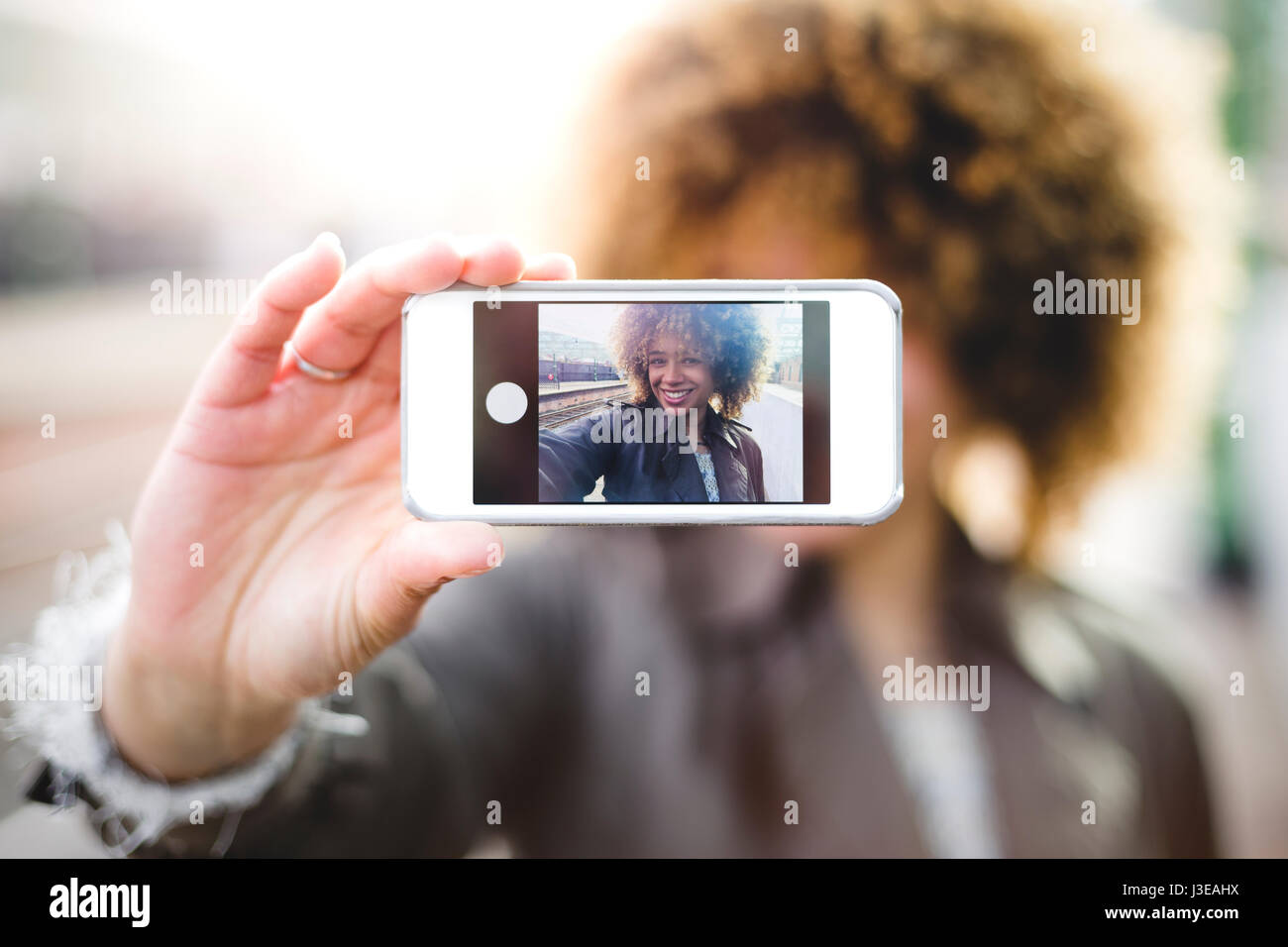 Prendre une femme sur un smartphone selfies. Elle est à l'extérieur et l'écran du téléphone peut être vu. Banque D'Images