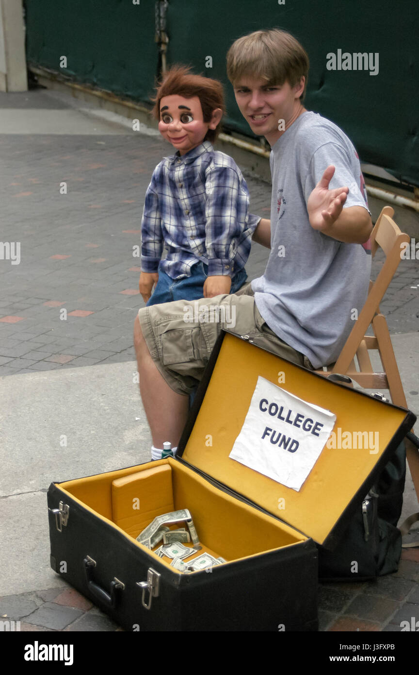 Un Caucase teenage boy sur une rue de la ville de New York avec un ventriloque, l'exécution. Son don tronc a un panneau qui dit "college fund'. Banque D'Images