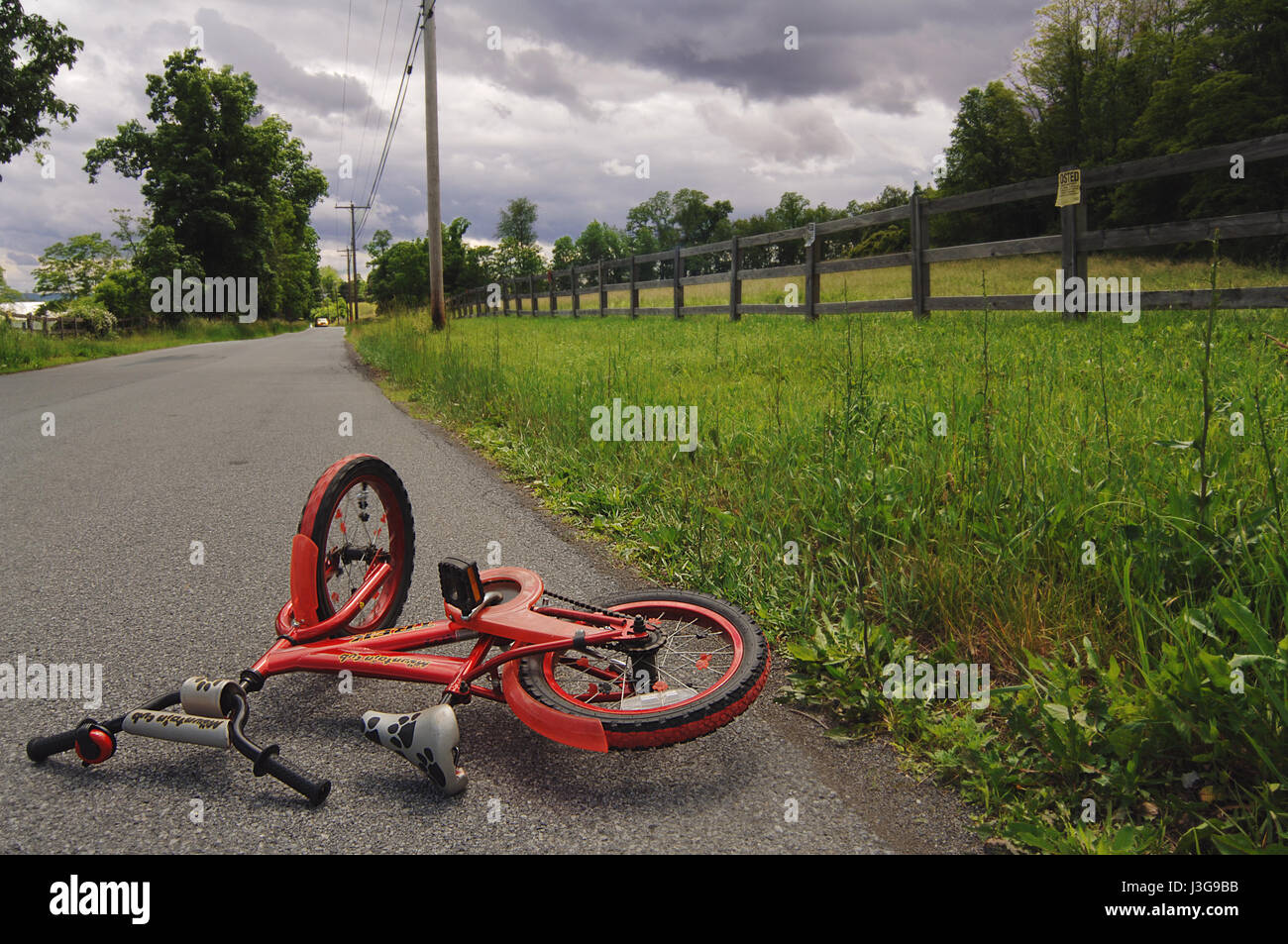 Red bicyclette d'enfant couché sur une route rurale représente les dangers des enfants à vélo sans casque Banque D'Images