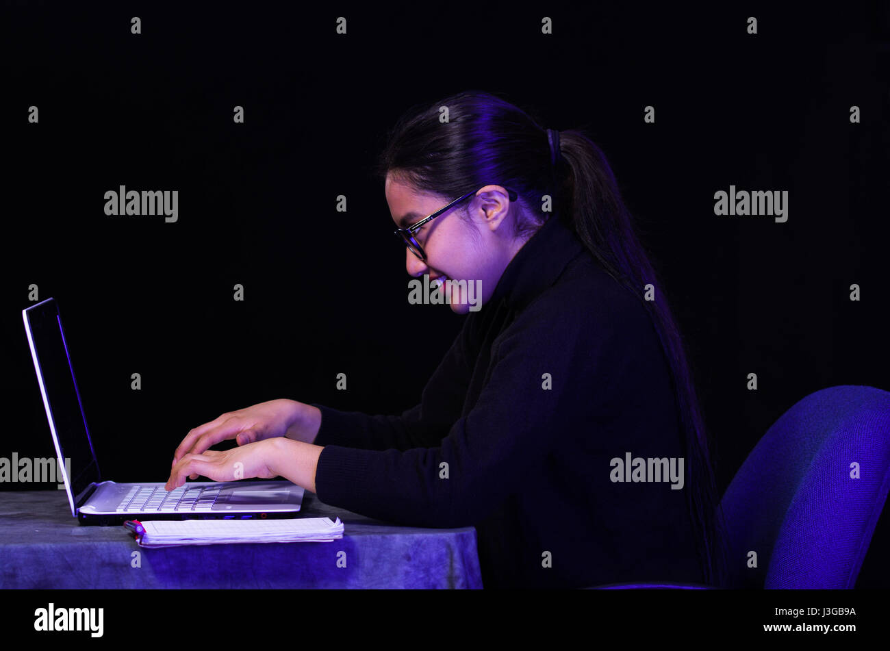 Portrait d'une belle, heureuse et smart girl travailler avec son ordinateur portable sur fond sombre à l'aide de verres Banque D'Images