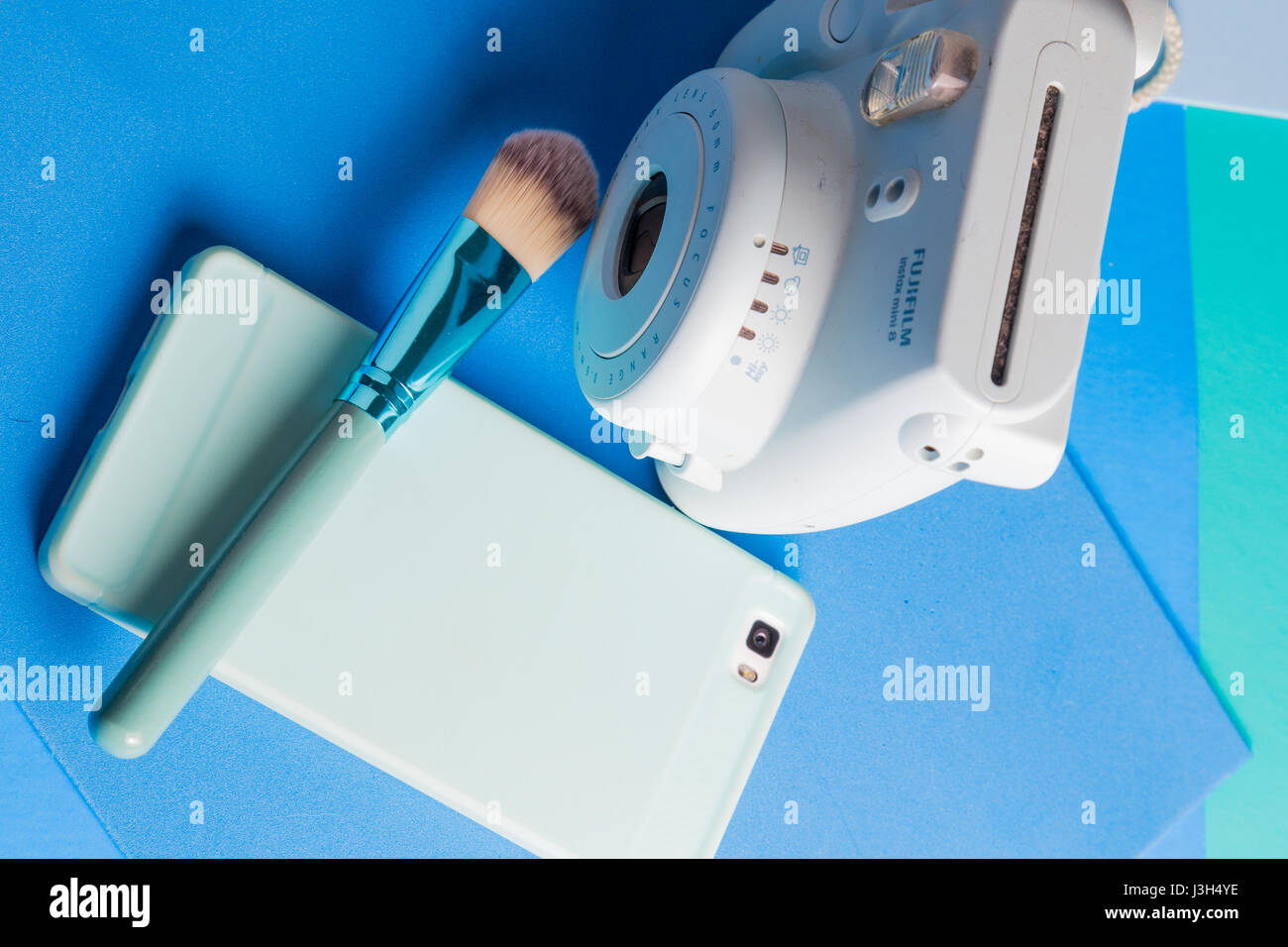 Sa vie sur des tons bleu : un appareil photo instantané, smartphone et un pinceau de maquillage placés dans un bleu de couleur Banque D'Images