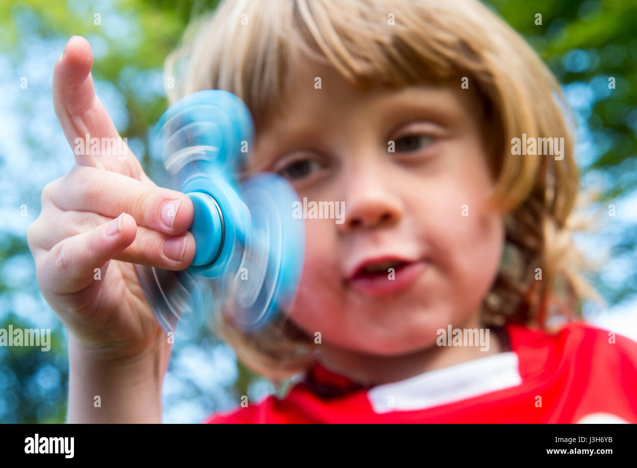 Un jeune garçon dans un uniforme de l'école rouge joue avec un bleu fidget spinner toy Banque D'Images