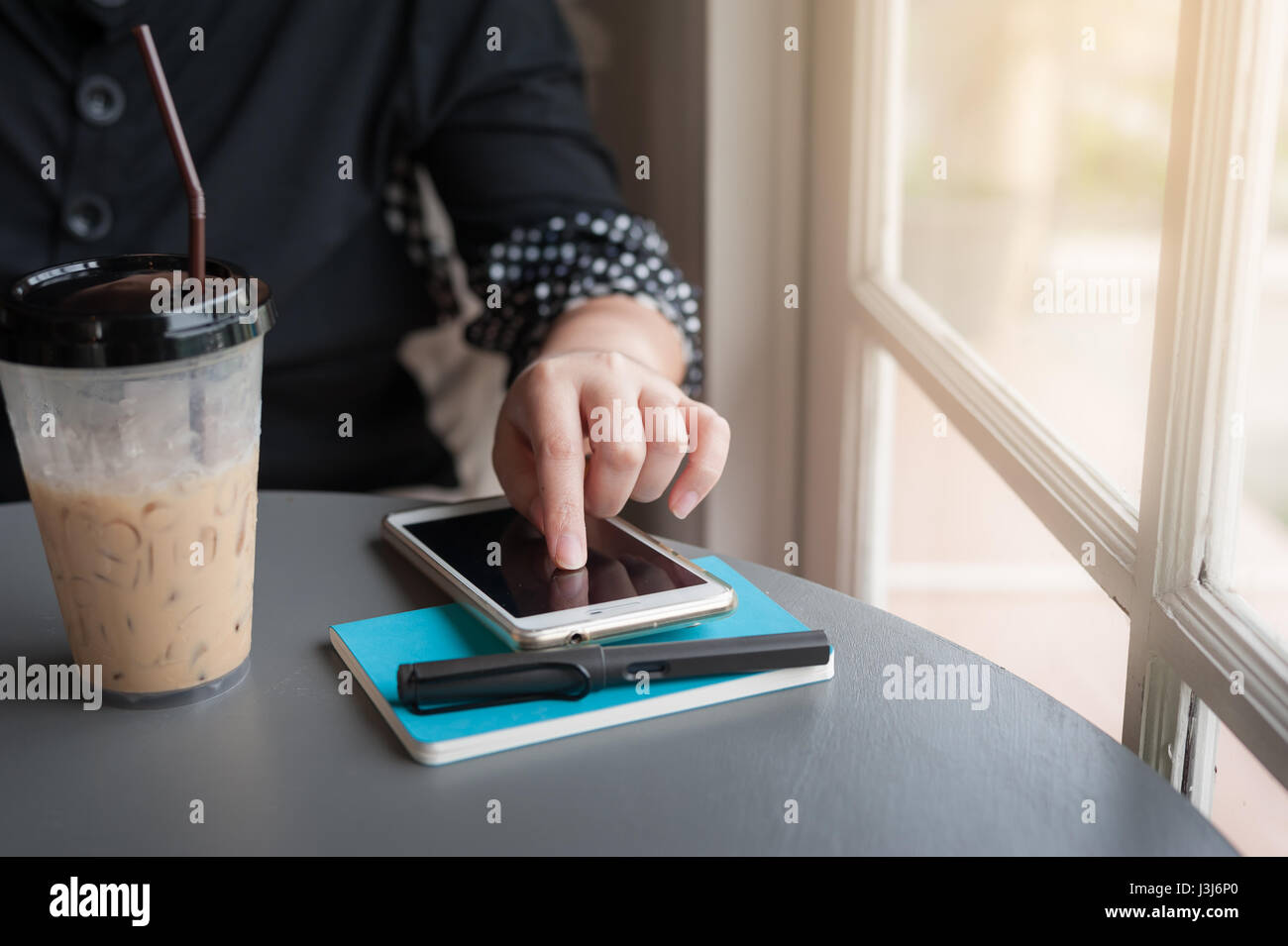 Woman using smartphone pour vérifier son programme avant d'écrire une note à l'ordinateur portable dans un café. Offres de travailler à partir de n'importe où concept Banque D'Images