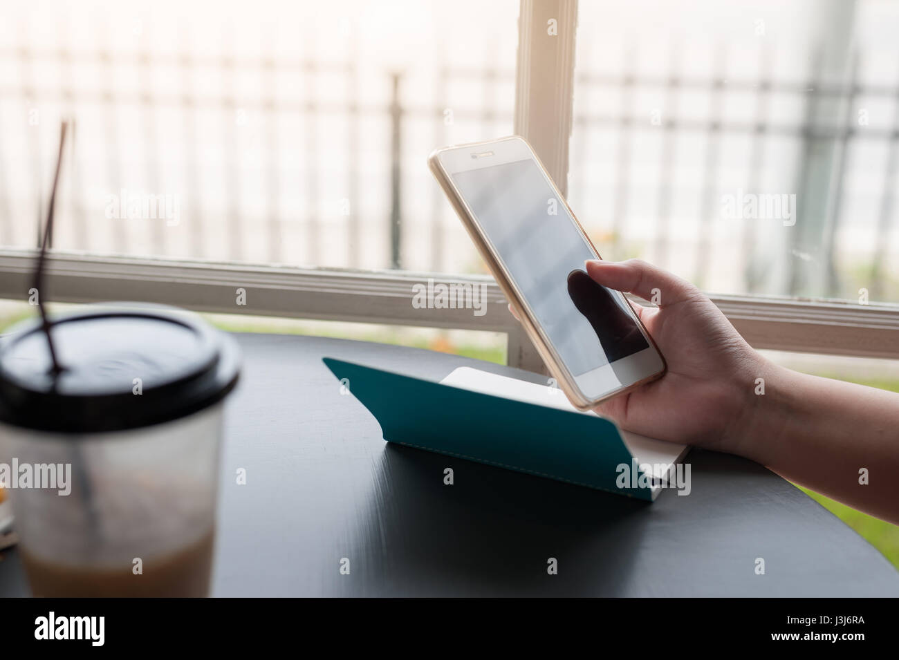 Woman holding smartphone à côté fenêtre avec tasse à café et petit carnet sur la table Banque D'Images