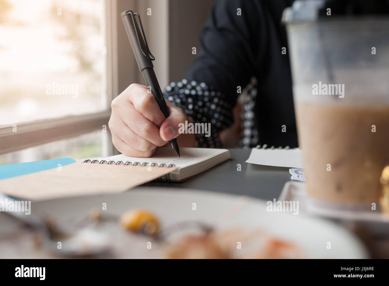 Woman holding pen lors de l'écriture sur le petit carnet à côté de fenêtre. Journaliste indépendant travaillant à domicile concept. Banque D'Images