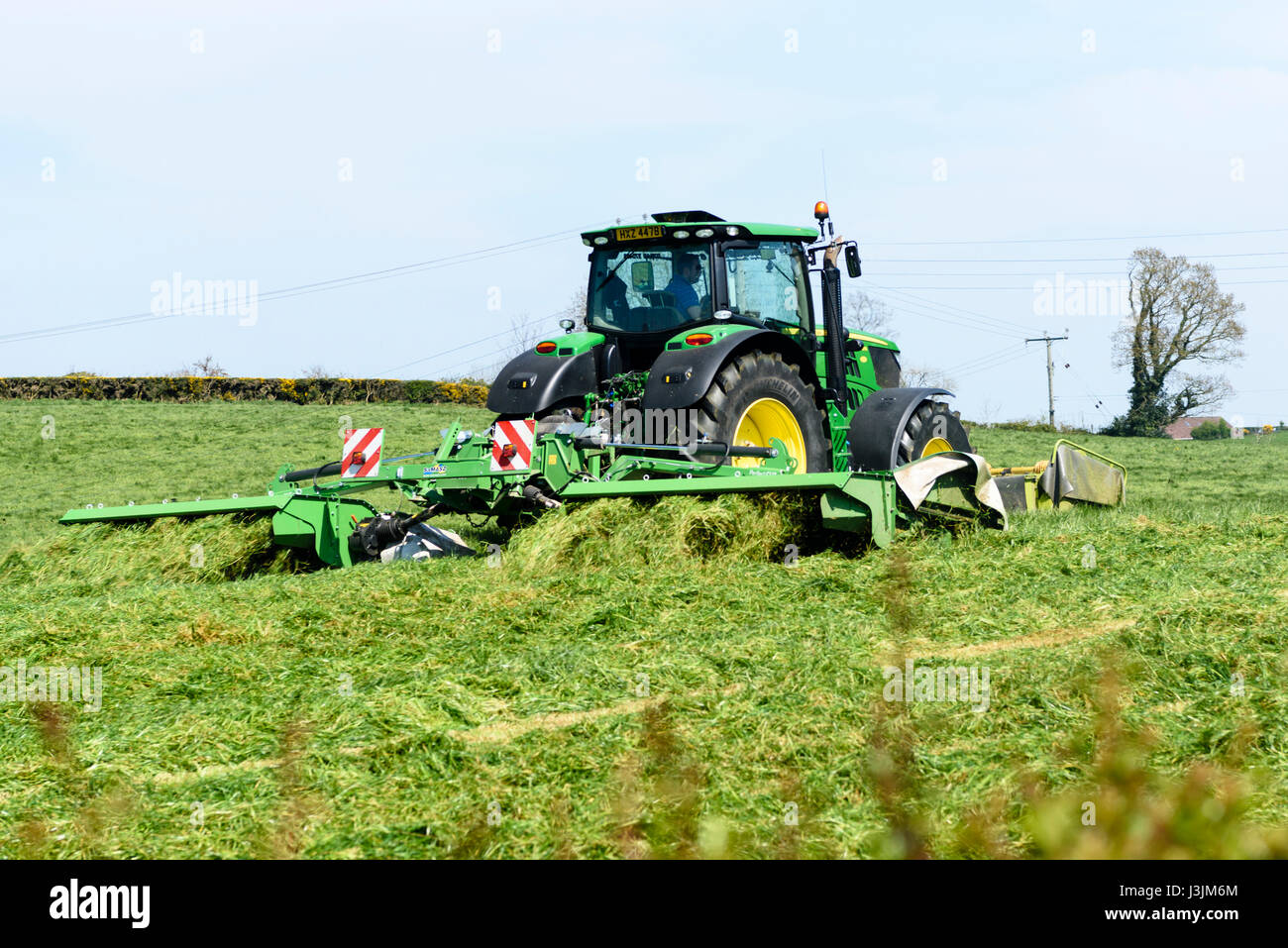 Fermier dans un John Deere 6190 avec disque avant et arrière coupe-herbe coupe la première récolte de l'ensilage. Banque D'Images