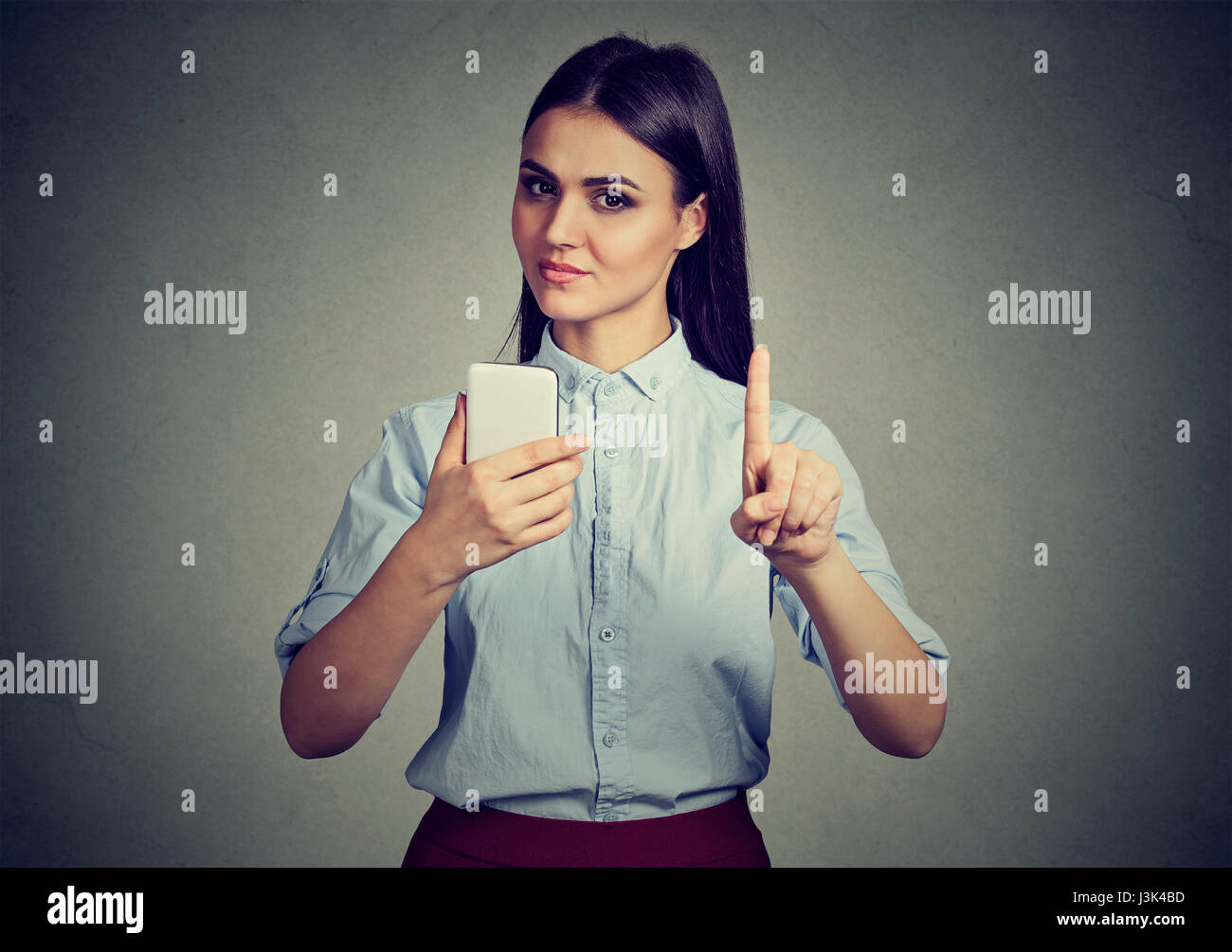 Jeune femme stricte avec le smartphone montrant pas, ne le faites pas, l'attention avec le doigt geste de la main. Le blocage de contenu adultes, concept de contrôle parental Banque D'Images