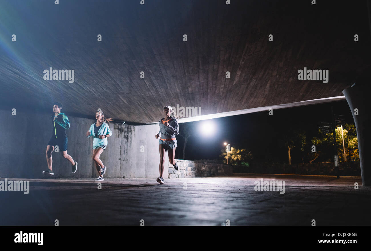 Une jeunesse saine fonctionnant sous un pont dans la nuit. Groupe de coureurs de la formation dans la ville. Banque D'Images