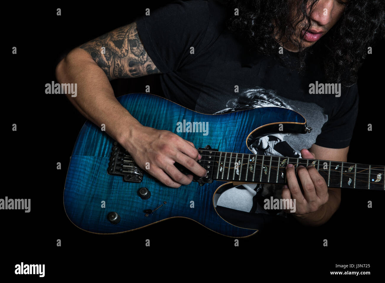 Jeune homme avec de longs cheveux bouclés jouer a blue guitare électrique. Banque D'Images