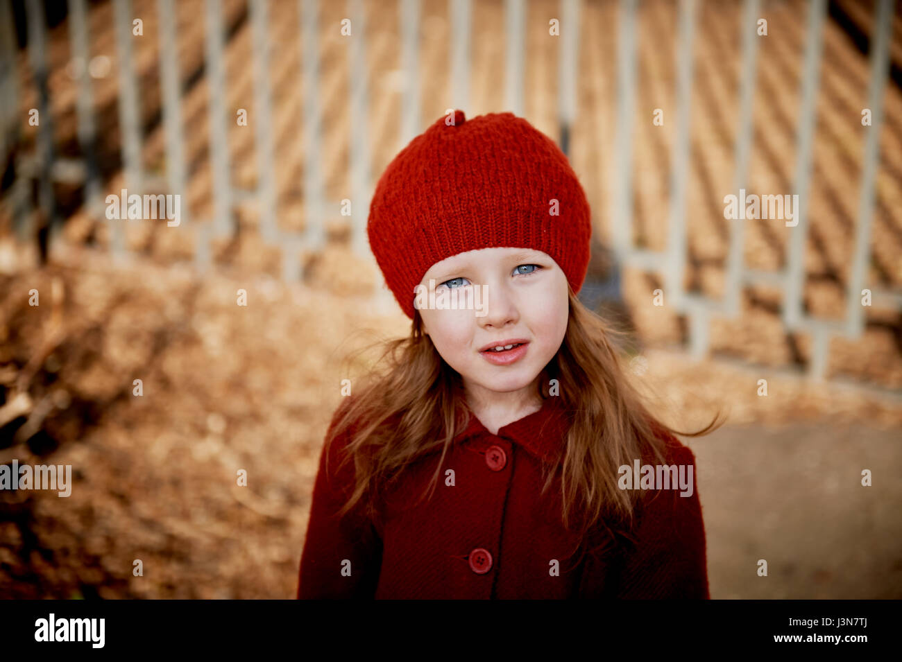 Bébé 3 ans avec des cheveux longs.Dans un béret rouge et portes manteau sur  la rue au soleil, près de la clôture Photo Stock - Alamy