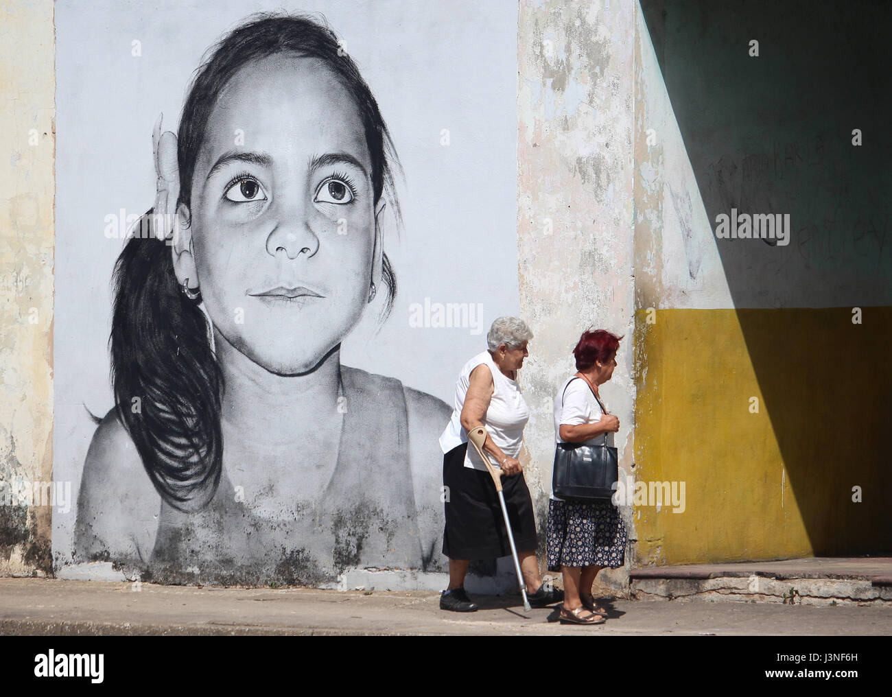 La Havane, Cuba. Apr 24, 2017. Deux femmes devant une image à grande échelle montrant le visage d'un enfant qui a été peinte sur un mur à La Havane, Cuba, 24 avril 2017. Artiste de rue Maisel Lopez tire de grands visages d'enfants sur les murs. Avec 'Los Colosos', le peintre cubain souhaite rendre l'art dans la rue. Photo : Guillermo Nova/dpa/Alamy Live News Banque D'Images