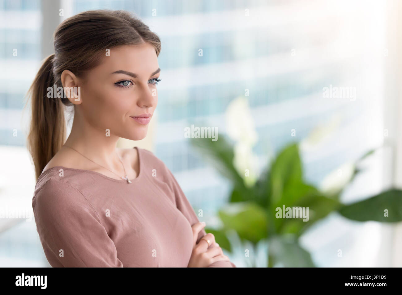 Pensive young woman looking through window, bras cros Banque D'Images