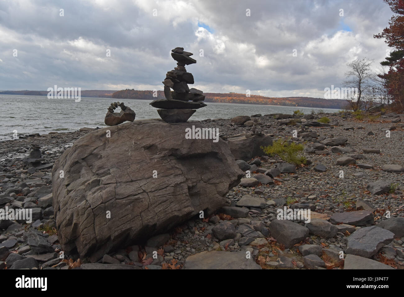 Sculptures en pierre sur plage rocheuse avec moody sky over lac lumineux Banque D'Images