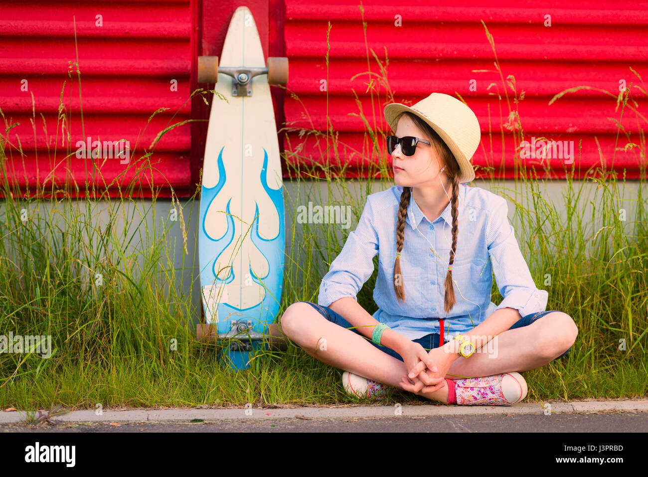 Jeune fille hipster avec tresses en lunettes de soleil et chapeau de paille  assis près de mur rouge vif et longboard Photo Stock - Alamy