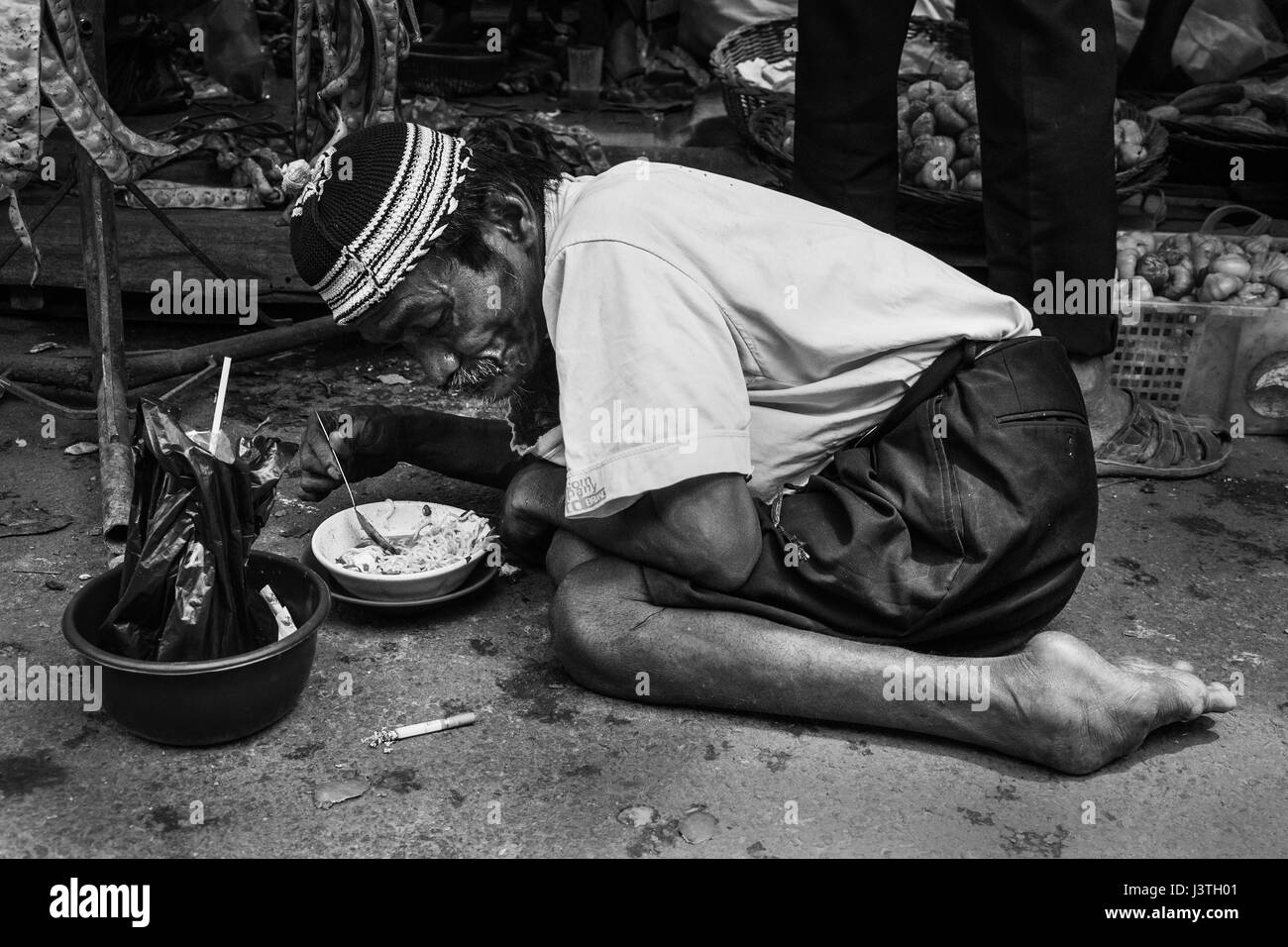 Portrait noir et blanc d'un pauvre vieil homme handicapé nouilles manger sur un terrain sur un marché à Sumatra Banque D'Images