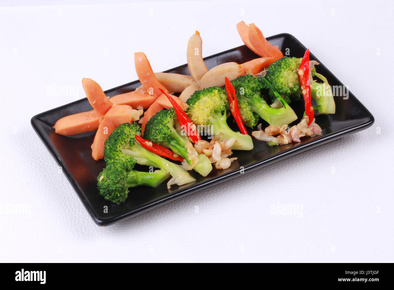 Le brocoli frits avec de la saucisse en sauce aux huîtres en japonais servi sur plat noir en cuir blanc. Banque D'Images