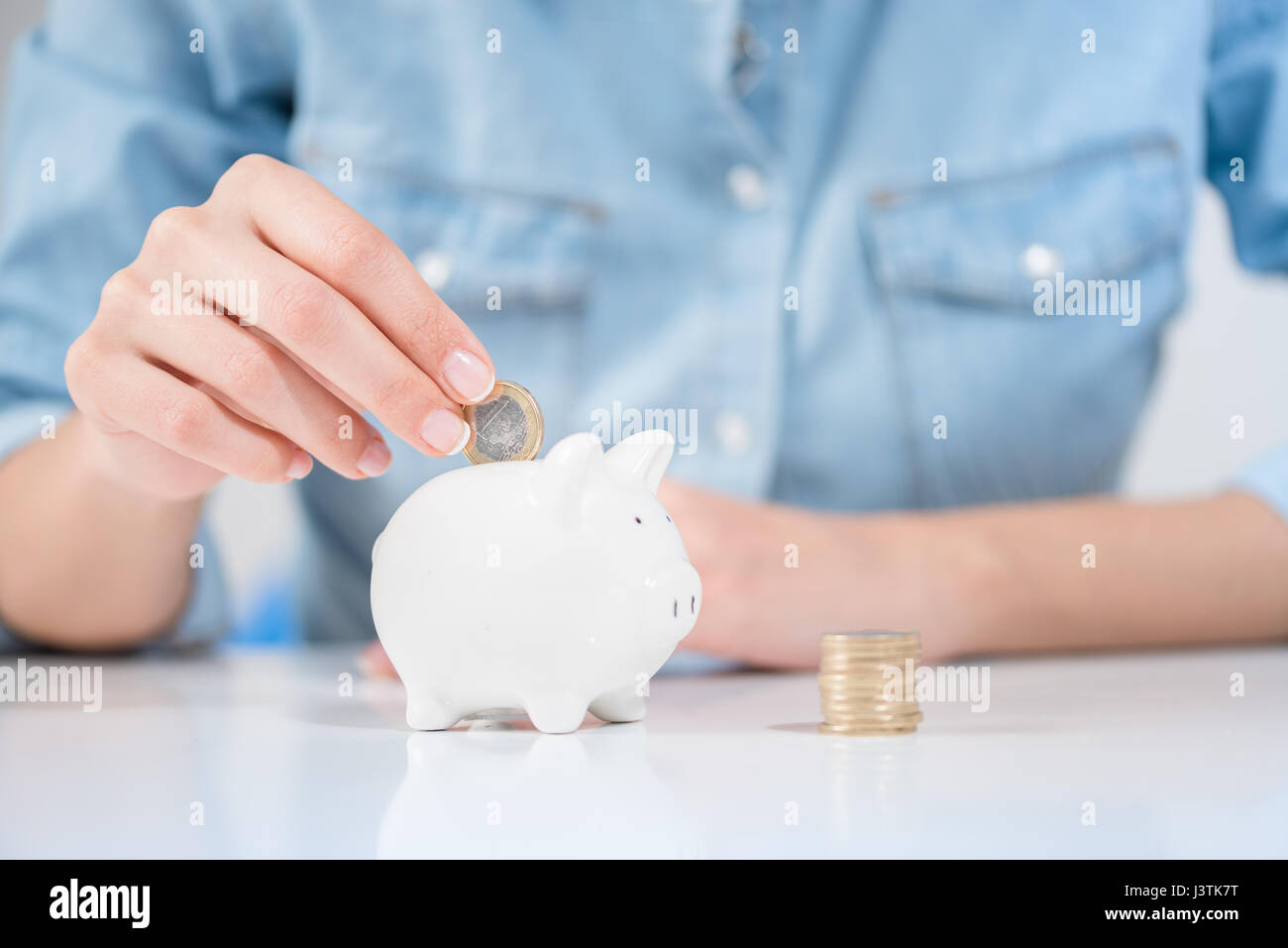 Woman Putting Coins In Piggy Bank, à l'intérieur Banque D'Images