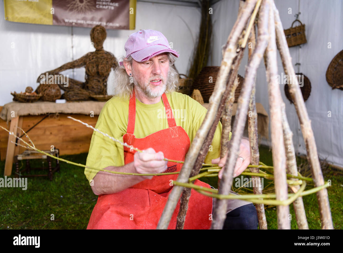 Un mâle weaver commence le tissage willow autour d'un cadre en bois Banque D'Images