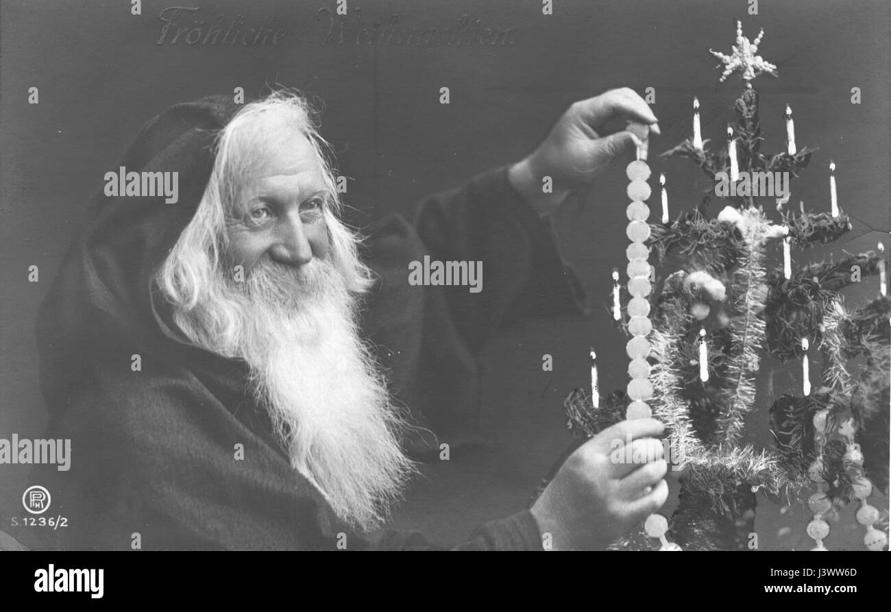 Souriant, gai Père Noël (v.33), portant un cape à capuche, décorent un arbre de Noël avec une chaîne de perles. Notez qu'il y a des bougies allumées sur l'arbre. Arbre a une étoile inhabituelle sur le dessus et les guirlandes s'étrangler autour. Pour voir mes autres images de Noël, recherchez: Prestor millésime vacances Banque D'Images