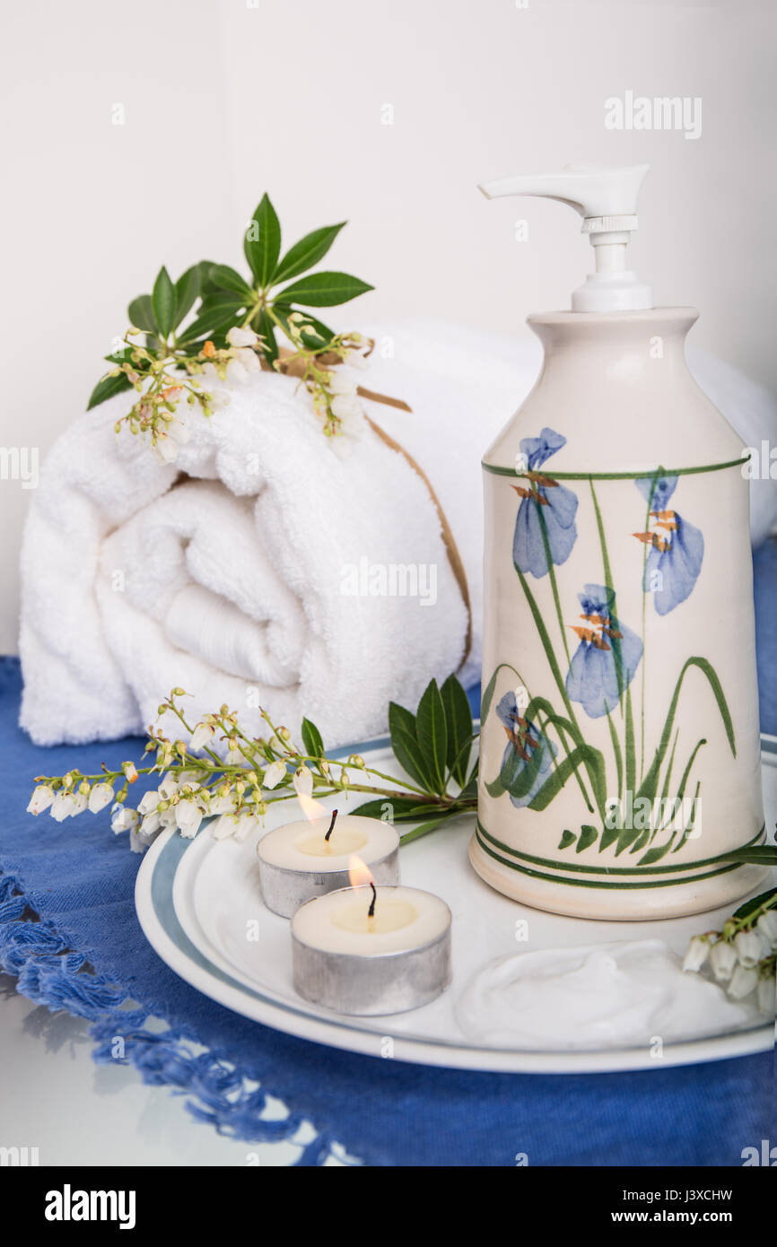 Lotion dans un joli récipient en poterie, entouré de Japonica, deux bougies thé et une serviette de bain Banque D'Images