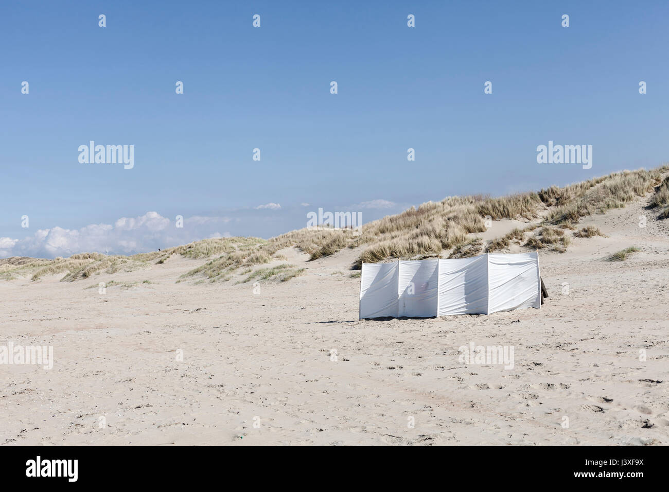 Oostduinkerke, Belgique - Touristes se cacher derrière un coupe-vent aux beaux mais jour de vent sur la plage à Oostduinkerke. Banque D'Images