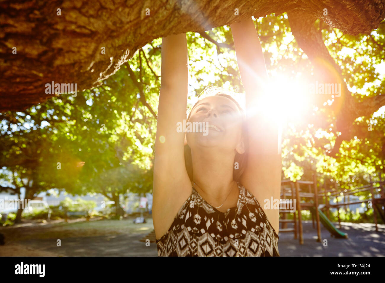 Girl hanging from tree branch, soleil qui brille à travers les arbres Banque D'Images