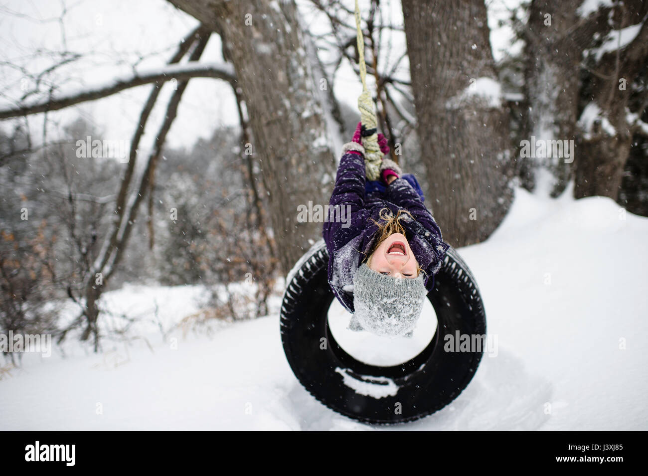 Jeune fille à l'envers sur balançoire pneu dans la neige Banque D'Images