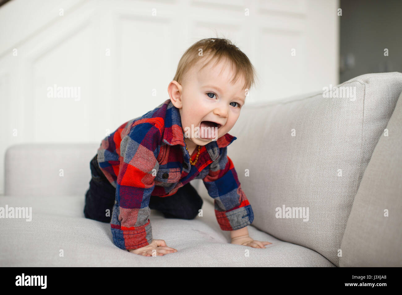 Portrait of male toddler crawling sur canapé sticking out tongue Banque D'Images
