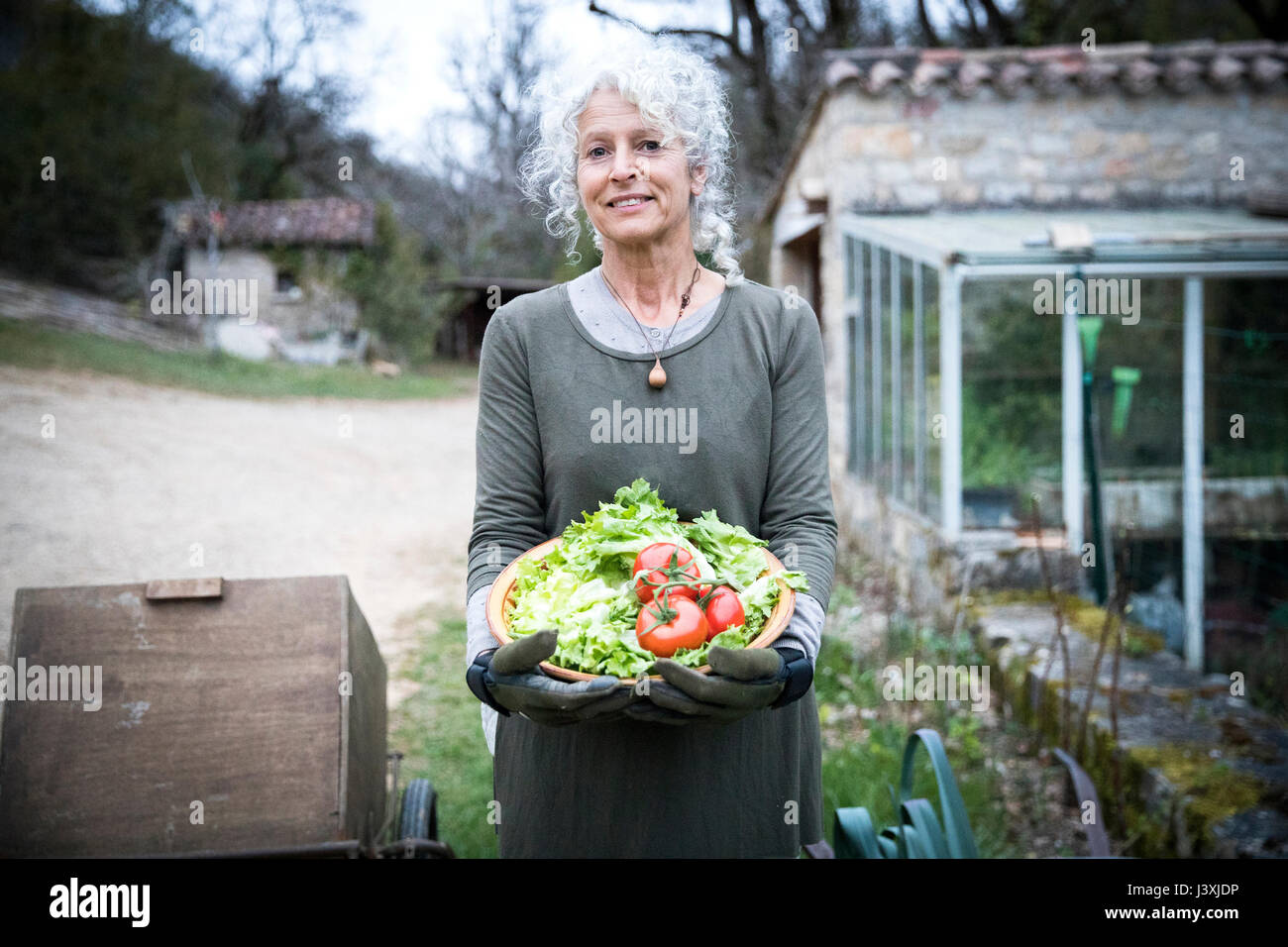 Portrait of mature female gardener avec bol de tomates et verts de printemps Banque D'Images
