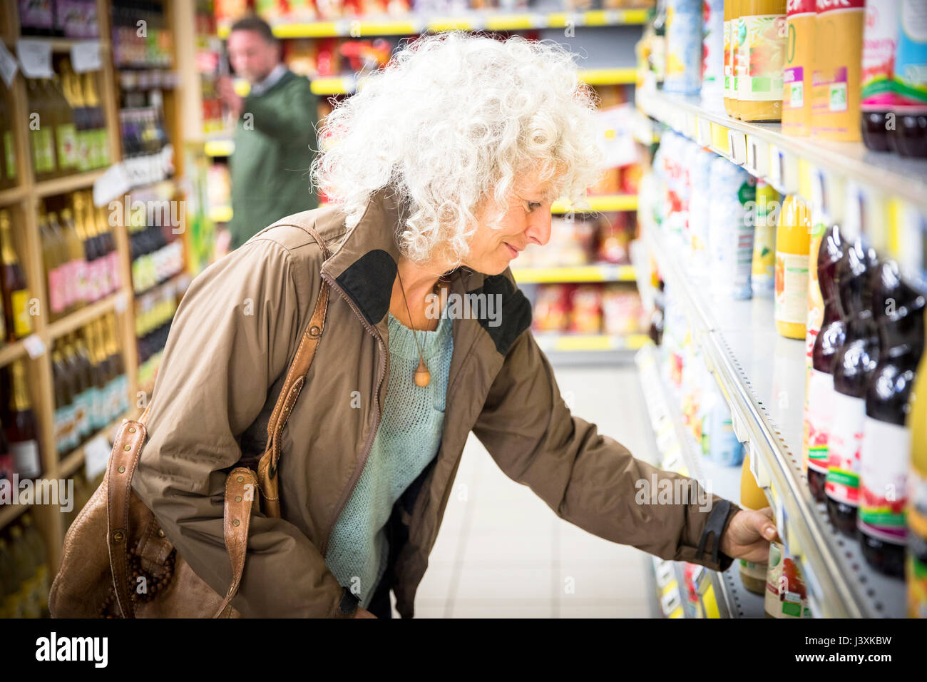 Femme mature en supermarché, en tenant une bouteille de jus à partir d'étagère Banque D'Images