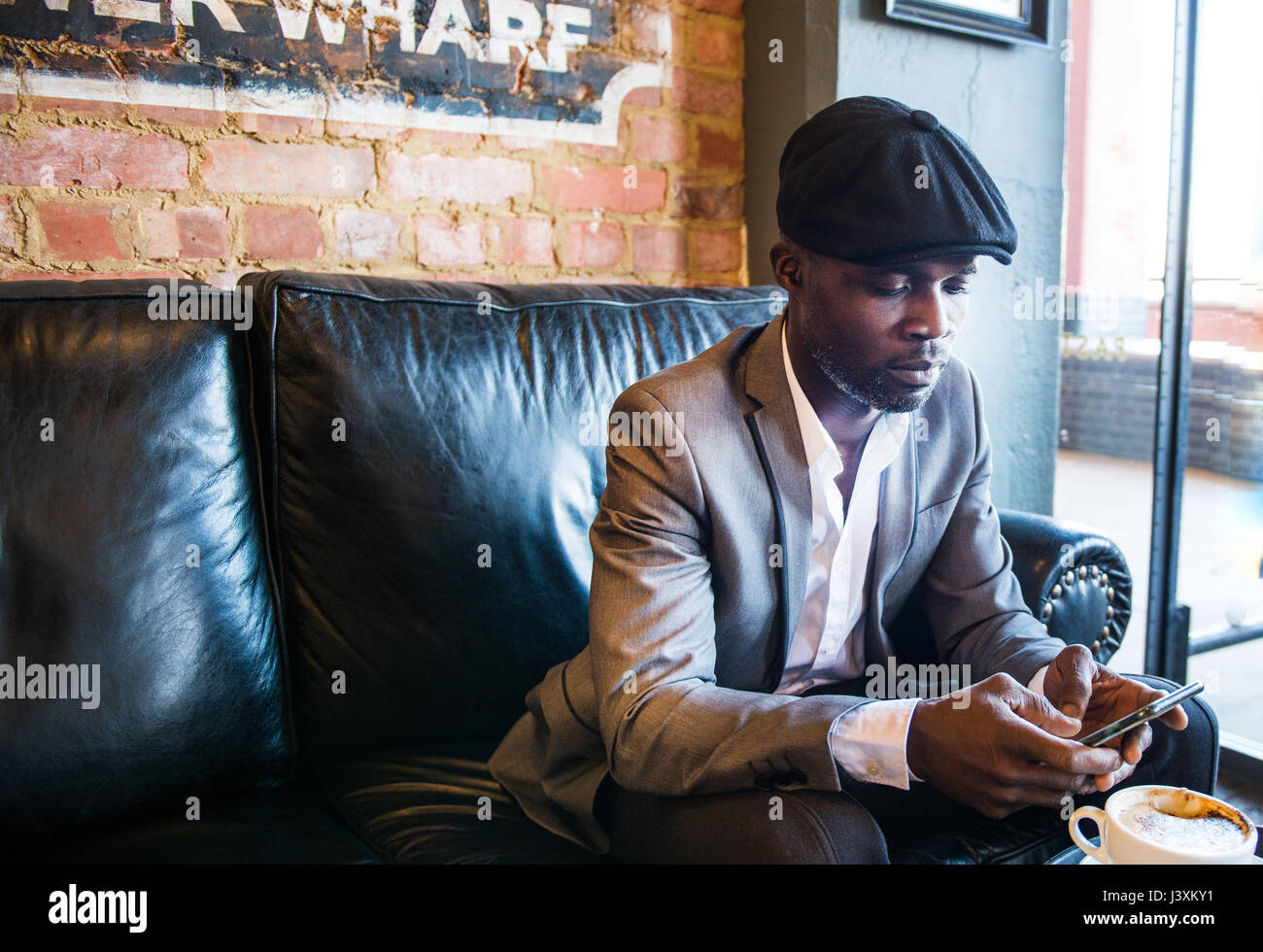 Businessman texting on sofa in cafe, London, UK Banque D'Images