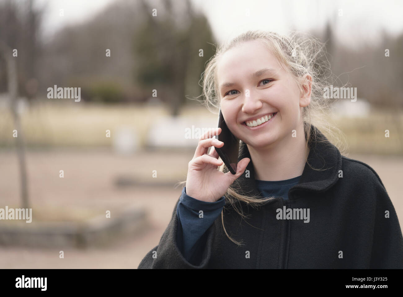 Teen girl debout sur le trottoir et à parler au téléphone au début du printemps Banque D'Images