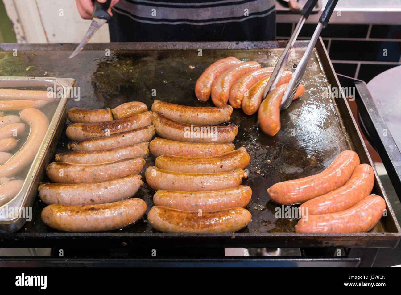 Man cooking sausages sur une grille dans un marché Banque D'Images