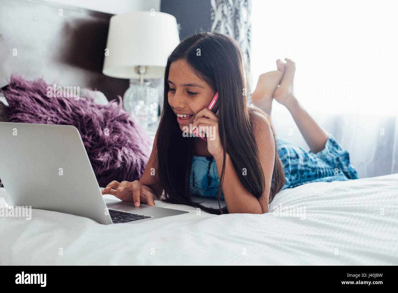 Girl lying on bed using smartphone et ordinateur portable Banque D'Images