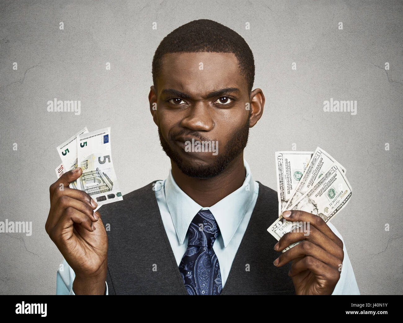 Closeup portrait confus, business man holding, dollar et euro factures en mains, isolé gris, fond noir. Taux de change bancaire conce Banque D'Images