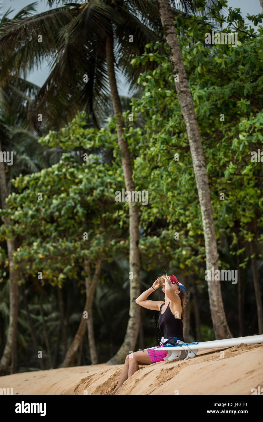 Jeune femme surfer assis sur la plage et boire d'une noix de coco, Sao Tomé, Sao Tomé et Principe, Afrique Banque D'Images