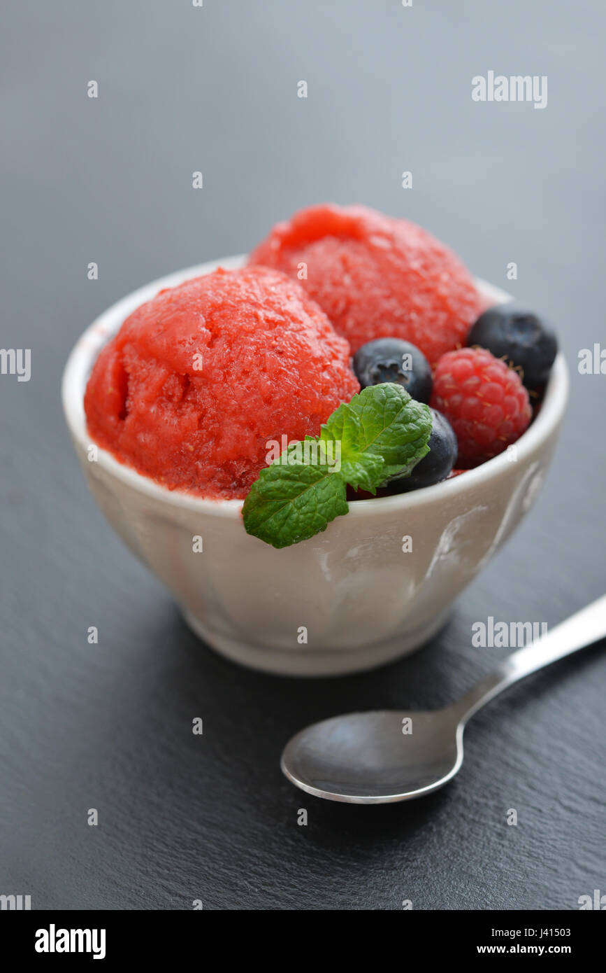 Fruit sorbet à la fraise à la framboise, myrtille et la menthe dans un bol sur fond d'ardoise noire Banque D'Images