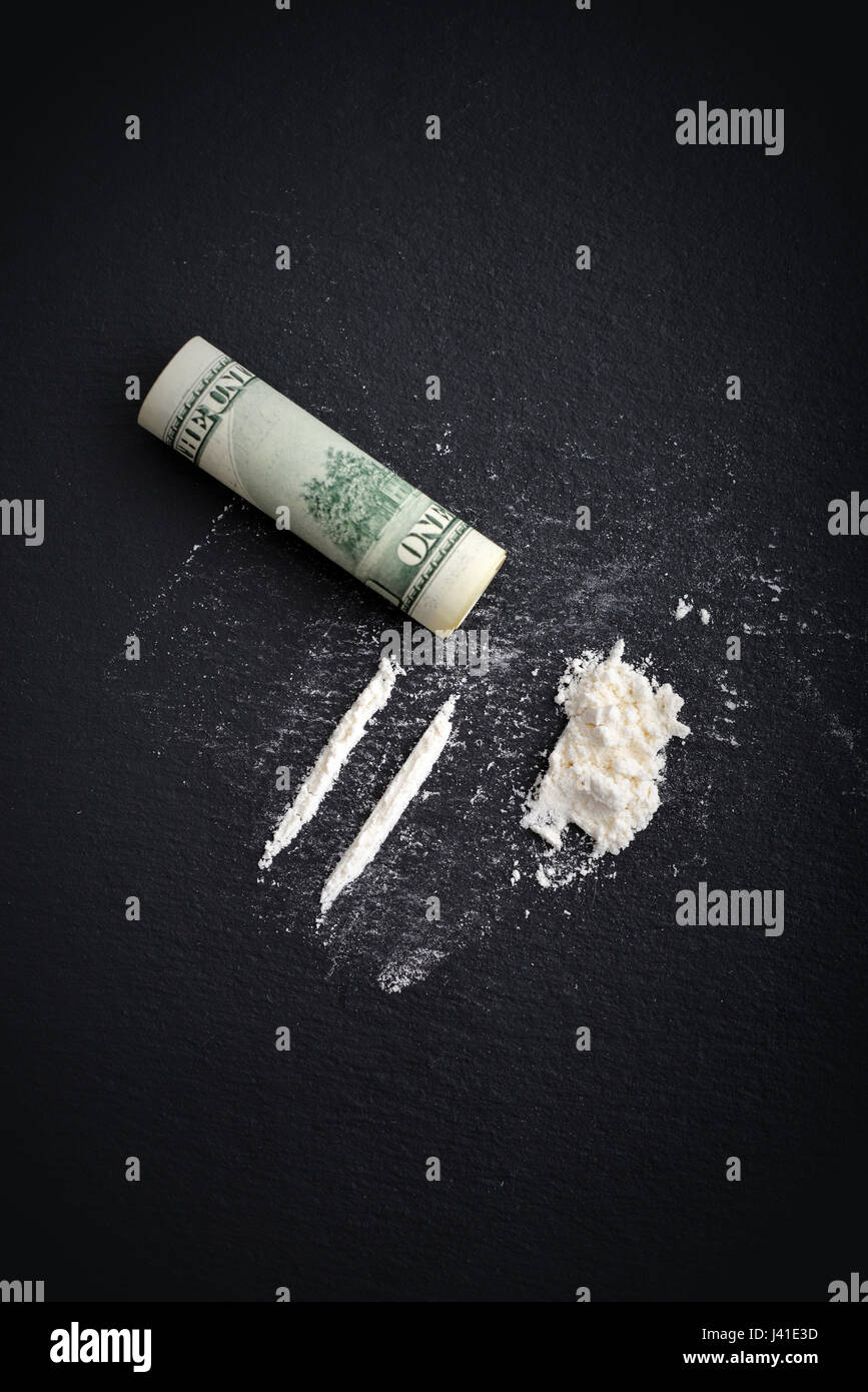 La toxicomanie à la cocaïne. Lignes de cocaïne et cent dollars billet sur fond noir Vue de dessus Banque D'Images