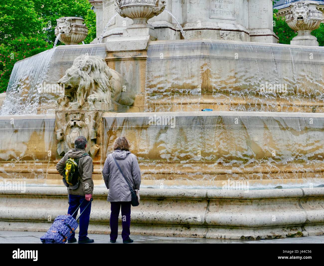 Couple wearing rain jackets et tirant à la valise roulant à Fontaine Saint-Sulpice dans de la pluie. Paris, France Banque D'Images