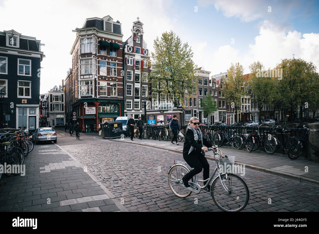 Amsterdam, Pays-Bas - 25 avril, 2017 : Adult woman rides un vélo dans la partie historique d'Amsterdam avec des maisons traditionnelles. Banque D'Images