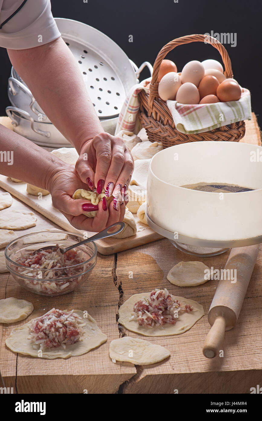 Femme avec de belles mains manucure pelmeni moule sur une table-top à partir d'un chêne Banque D'Images